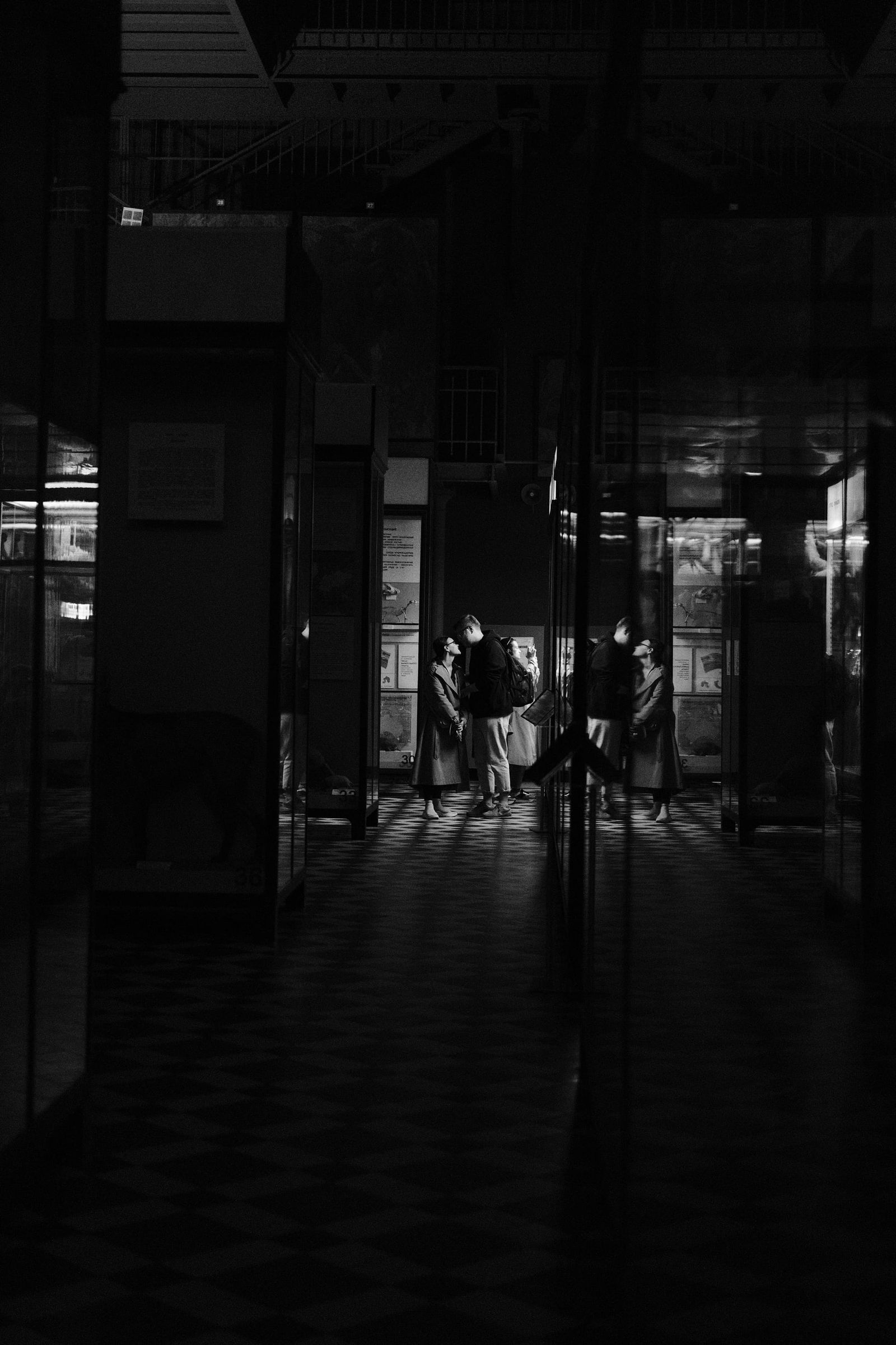 A dark museum corridor leads toward distant illuminated display cases and visitors.