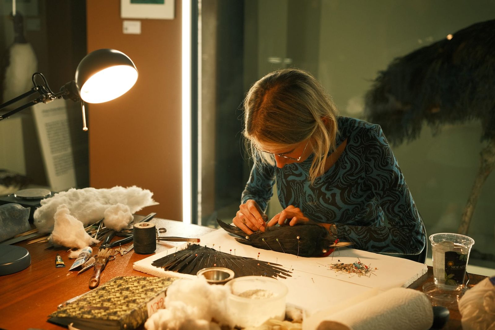 Close view of a woman working carefully at a museum bench covered with tools, materials and specimens.