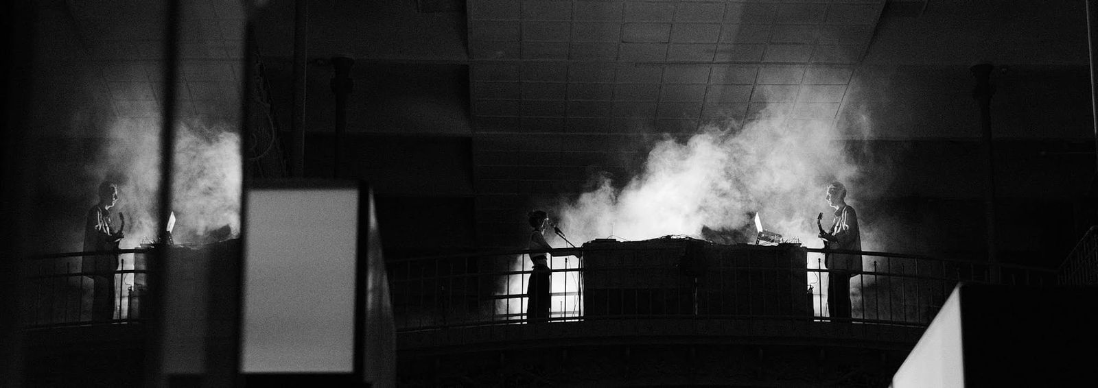 Black-and-white view across an interior balcony, with drifting vapour lit above the railing.