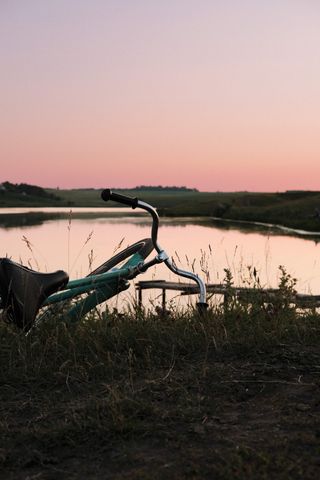 Bicycle beside a calm lake beneath a pastel pink and blue evening sky