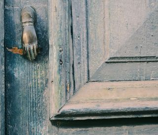 Close view of a weathered blue-green wooden door with a hand-shaped metal knocker.