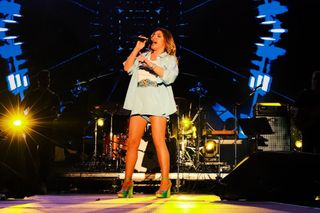 Helena Paparizou singing into a handheld microphone under blue and yellow stage lights.