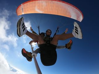 Tandem paragliding pair beneath an orange canopy against a deep blue sky