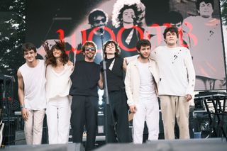 Six members of WOOMB standing together at the front of the outdoor festival stage.