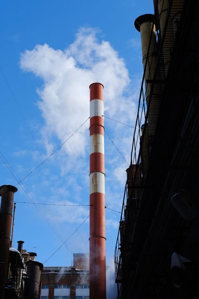 Red-and-white industrial chimney rising into a blue sky with white clouds in Moscow