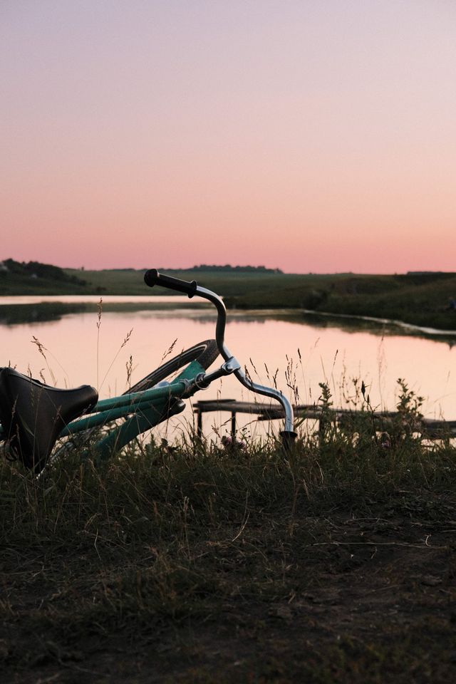 Bicycle beside a calm lake beneath a pastel pink and blue evening sky