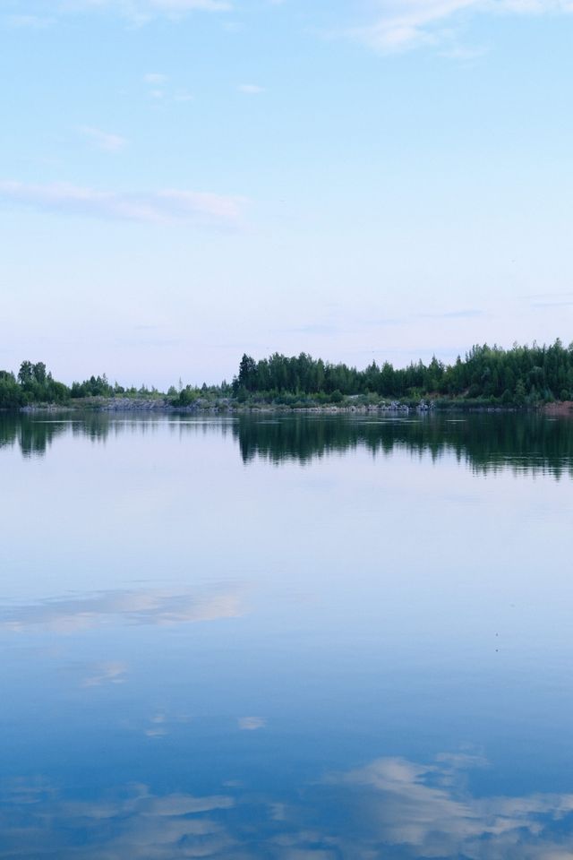 Calm lake reflecting a soft blue and pink sky beside a dark tree line