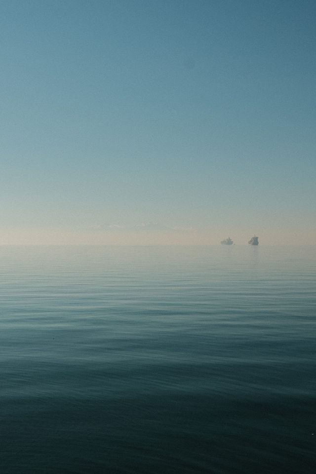 Calm Greek sea fading into a hazy blue horizon with two distant rocky islets