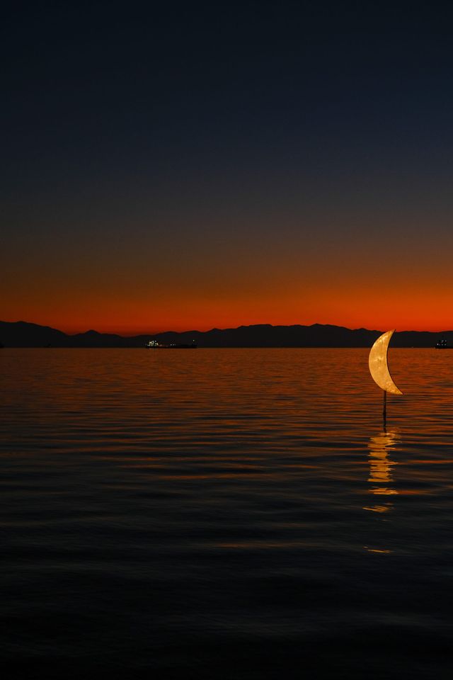 Crescent-shaped light reflected on calm water beneath a deep orange twilight sky