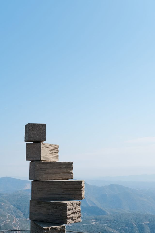 Stacked stone sculpture overlooking mountains beneath a clear pale blue sky