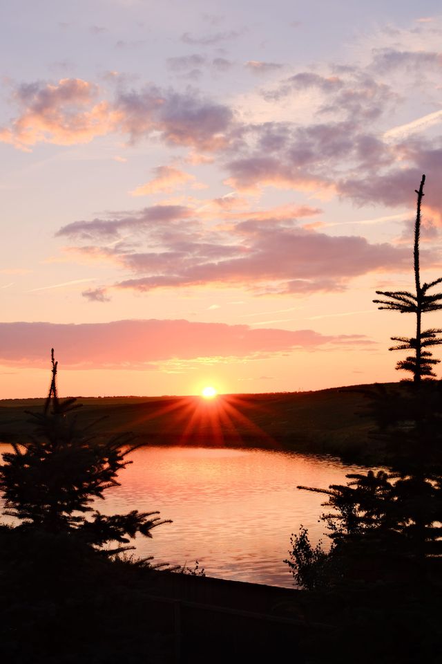 Sun setting over a small lake framed by dark evergreen trees