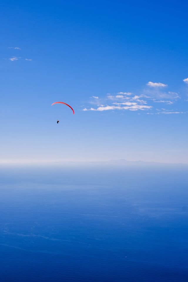 Paraglider suspended above a deep blue sea beneath a clear sky