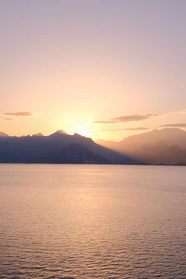 Golden sun sinking behind mountain silhouettes across calm water