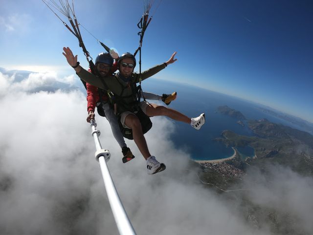 Tandem paragliding pair above white cloud with the coast below