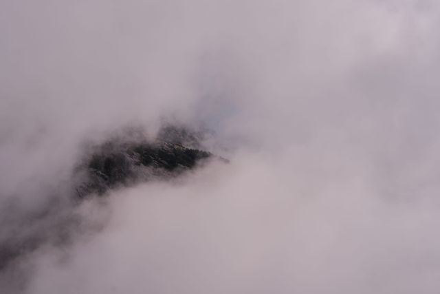 Dense white cloud opening briefly over the rocky mountainside