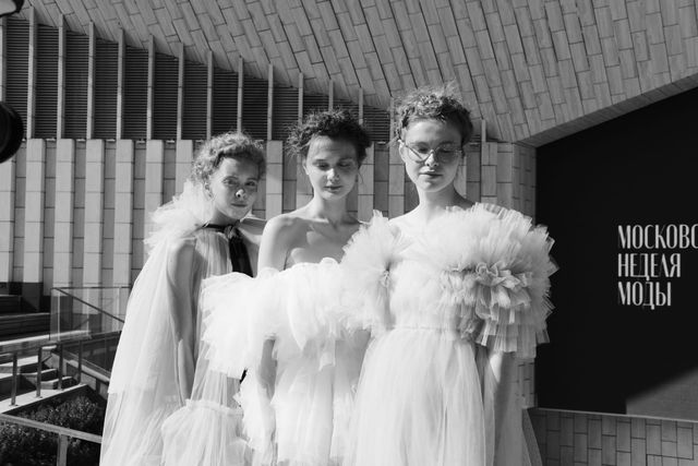 Black-and-white group portrait of three models in voluminous ruffled outfits outside the venue.