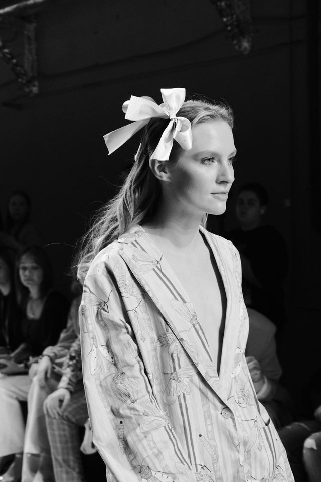 Black-and-white portrait of a runway model wearing a textured top and a large bow in her hair.