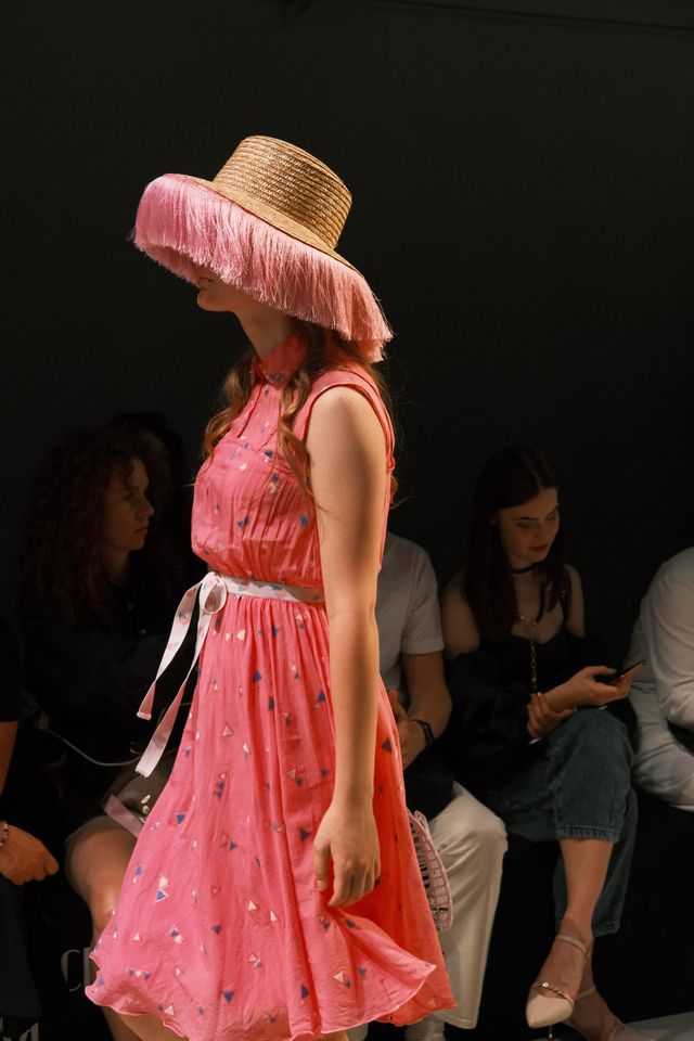 A model walks in a bright pink dress and a wide-brimmed hat with pink trim.