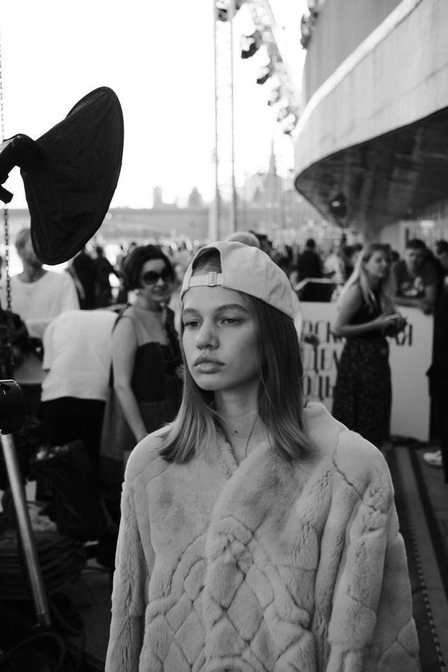 A model wearing a backward cap and a textured jacket approaches the camera in black and white.