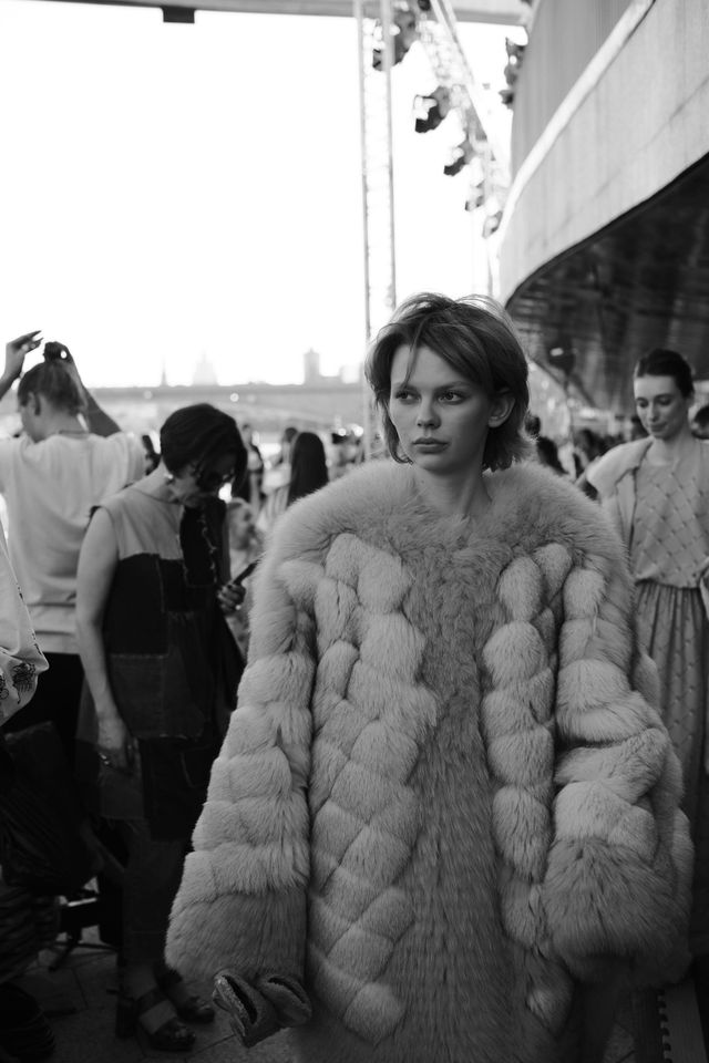 A model in a voluminous coat with large rounded textures walks past spectators in black and white.