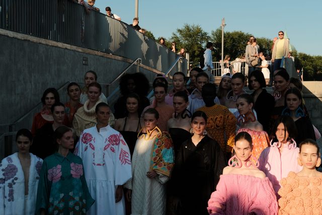 Models in colourful outfits gather on outdoor steps, with sunlight highlighting pink and white ruffles.