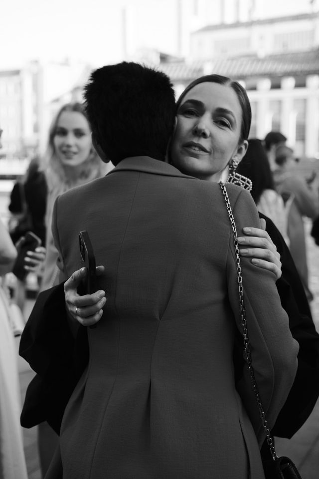 Two people embrace among the event guests in a black-and-white photograph.