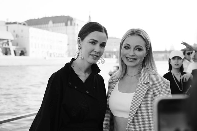 Two women smile beside the river in a black-and-white photograph, with a phone in the foreground.