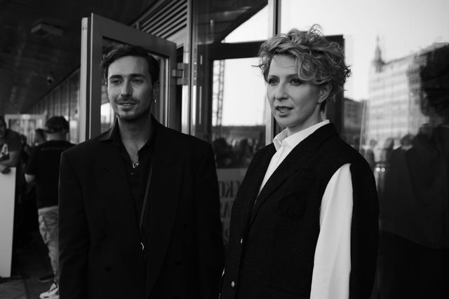 Black-and-white portrait of two guests, one in a dark jacket and the other wearing a white shirt under a dark sleeveless garment.