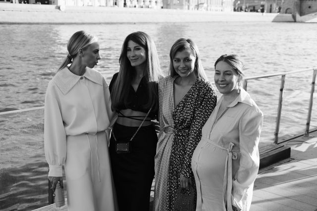 Four women pose together beside the river in a black-and-white photograph.