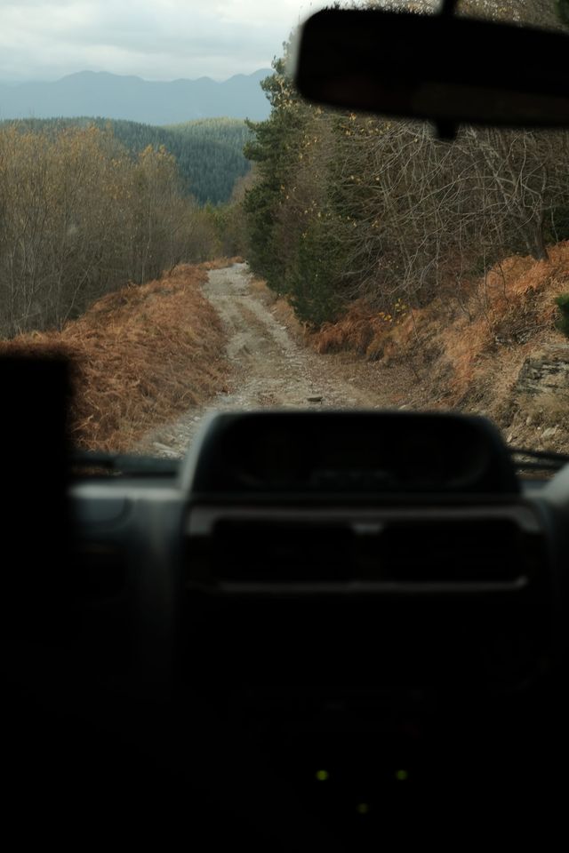 A rough mountain track seen through the windscreen above a dark vehicle dashboard.