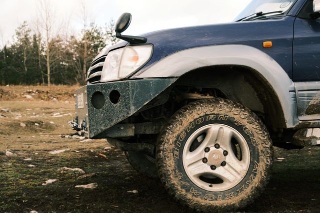 The front wheel and bumper of an off-road vehicle parked in a forest clearing.