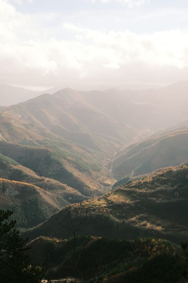 A tall view into a winding mountain valley, with warm light across successive ridges.