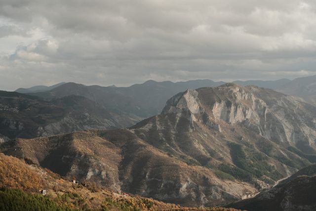 A pale, steep-sided mountain rises beneath dark clouds above surrounding forested ridges.