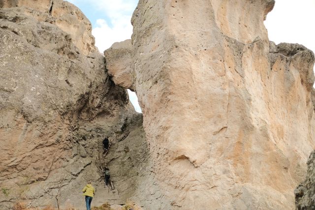 A small figure stands beneath towering pale rock walls separated by a narrow opening.