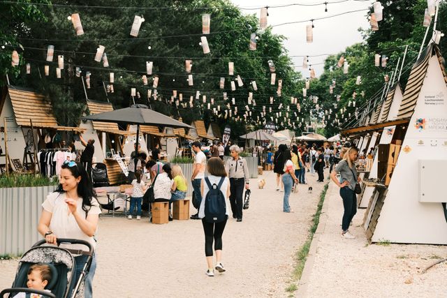 Visitors walk between outdoor food stalls beneath hanging decorations and trees.