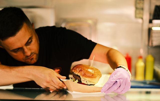 A cook leans over the counter to arrange a burger in its cardboard serving tray.