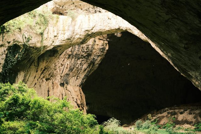 Massive shadowed entrance and limestone wall of Devetashka Cave