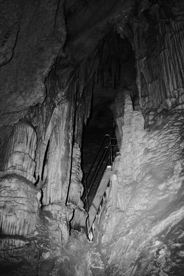 Tall stalactites and a staircase in a black-and-white cave chamber