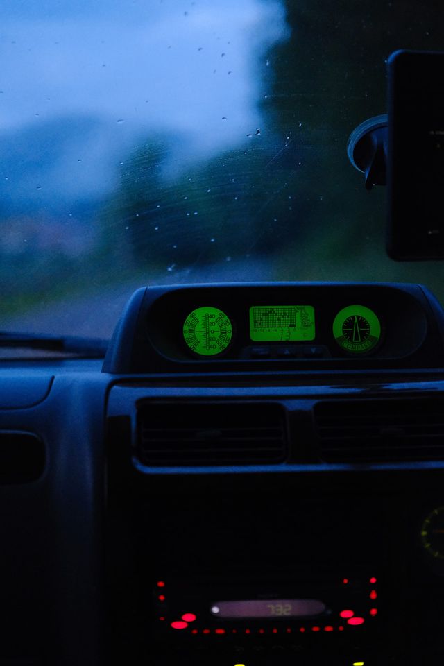 Car dashboard glowing green during a rainy twilight drive