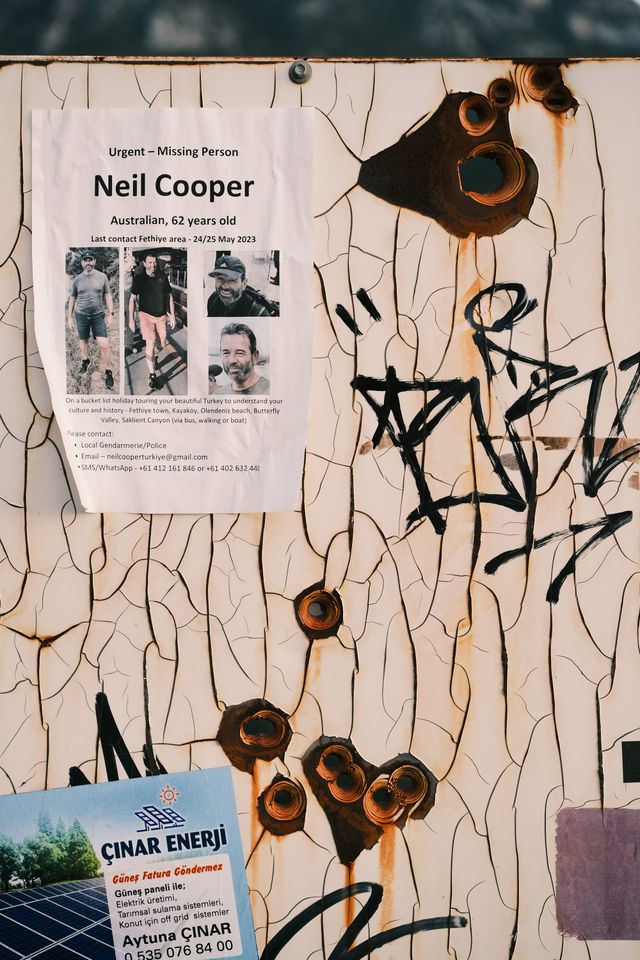 Memorial notice and stickers on a weathered, bullet-marked sign