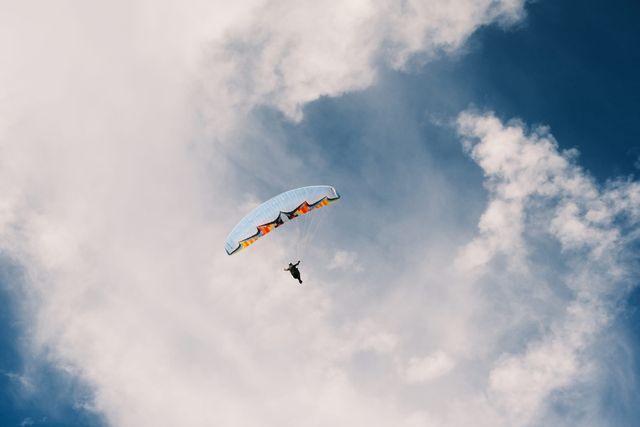Paraglider suspended in front of a large white cloud