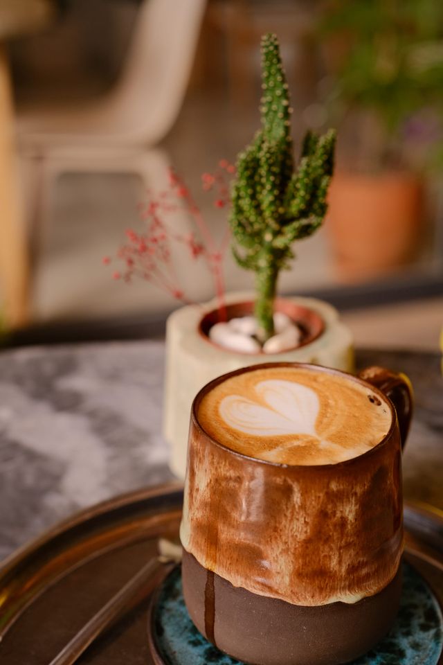 Latte in a handmade brown cup beside a small potted cactus