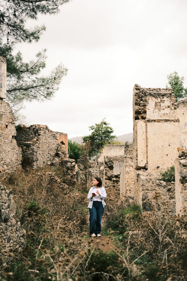 Person standing among overgrown stone ruins in Kayaköy