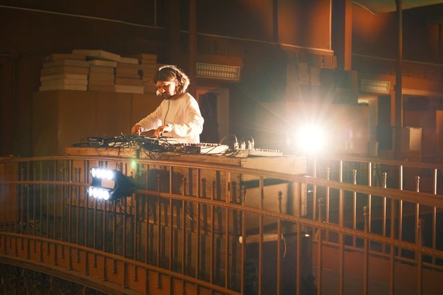 A person works behind a railing in a dim museum room, illuminated by a bright lamp.