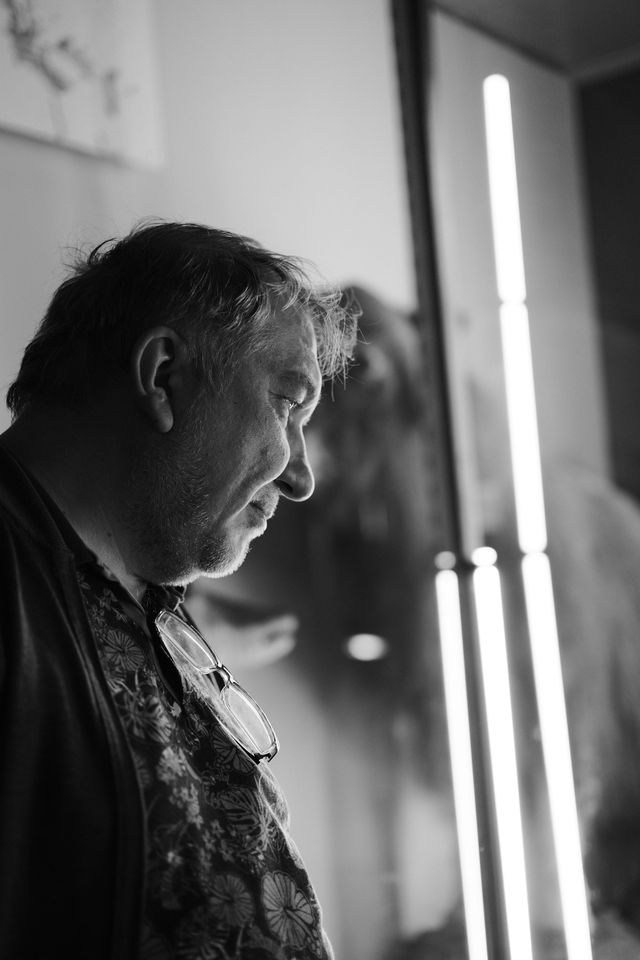 Black-and-white portrait of a man looking downward beside a brightly lit window.