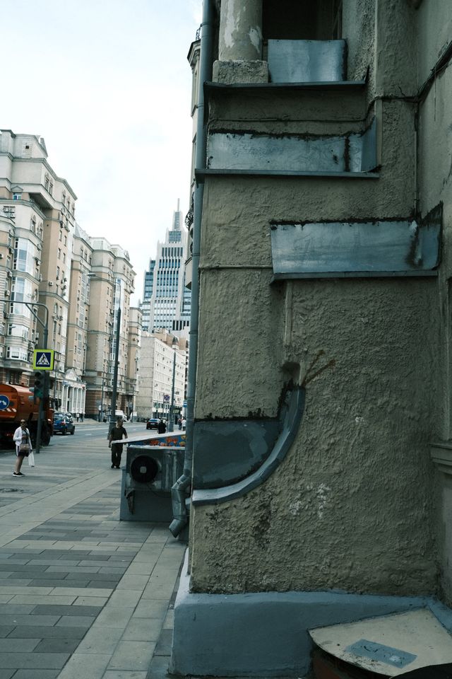A bent metal pipe fixed to a grey building corner beside a narrow Moscow street.