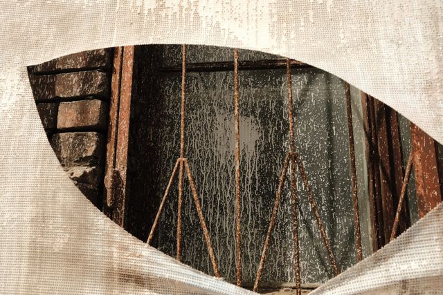 Torn white mesh reveals rusted metal bars and a dark window set in brickwork in Moscow.