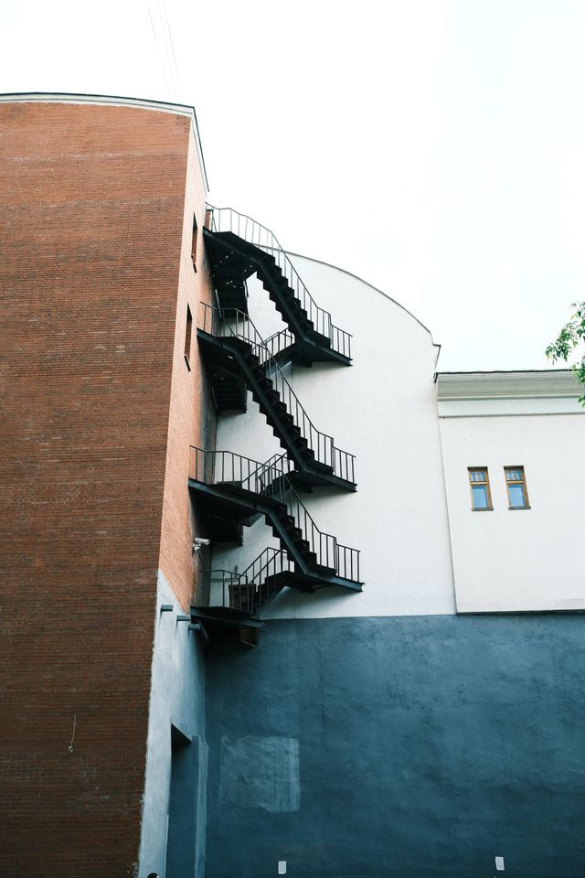 A black exterior fire escape zigzags between a red brick wall and a curved white facade in Moscow.