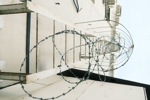 Loops of barbed wire project from a pale wall with metal brackets and an air-conditioning unit in Moscow.