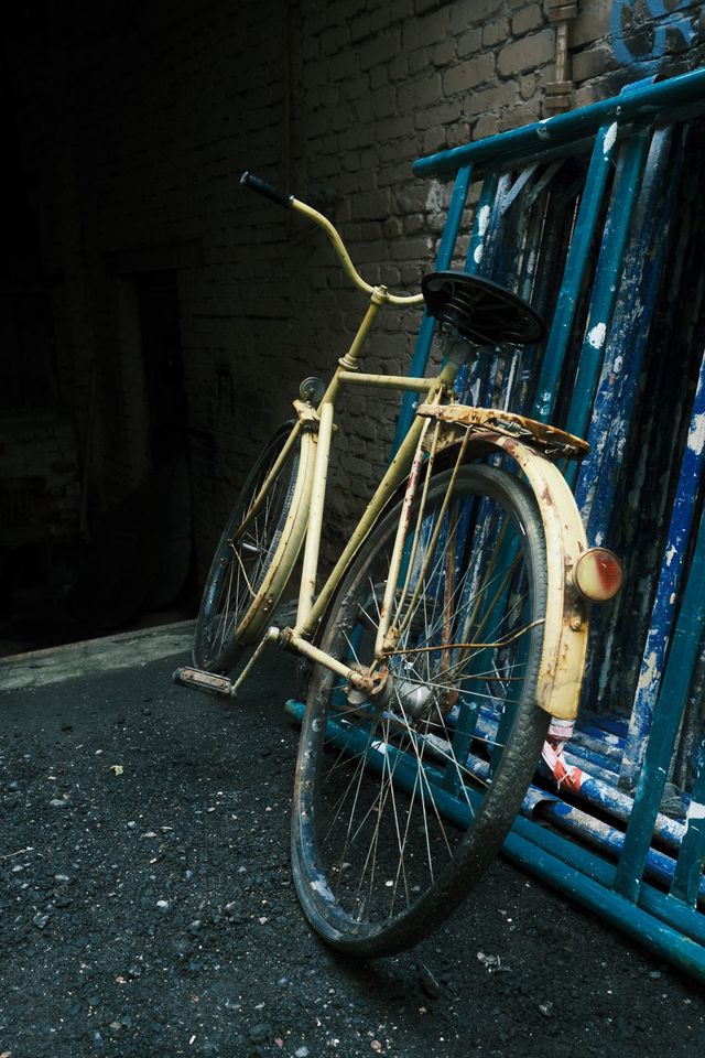 A worn yellow bicycle leans against blue wooden frames in a shaded Moscow courtyard.